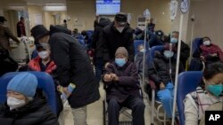 A man pushes an elderly woman past patients receiving intravenous drips in the emergency ward of a hospital, Jan. 3, 2023. 