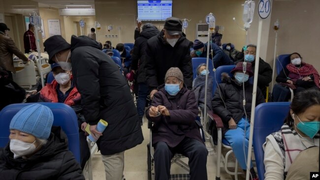 A man pushes an elderly woman past patients receiving intravenous drips in the emergency ward of a hospital, Jan. 3, 2023. 