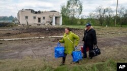 People walk with their belongings to an evacuation point, passing a building that was damaged by a Russian airstrike, in Vilcha, near Vovchansk, in Ukraine's Kharkiv region, May 12, 2024.