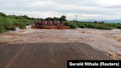 Des gens se tiennent de l'autre côté d'une route détruite par la tempête tropicale Ana, le long de la route M1 Chikwawa au Malawi, le 26 janvier 2022.