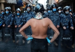 FILE - An anti-government protester stands in front of the Lebanese riot police who wear masks to help curb the spread of the coronavirus, during a protest over the deepening financial crisis in Beirut, Lebanon, April 23, 2020.