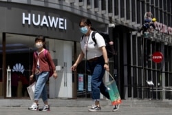 FILE - Residents wearing face masks to protect against the coronavirus walk past a Huawei retail store in Beijing, May 18, 2020.