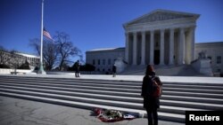 Flowers are seen as a woman stands in front of the Supreme Court building in Washington, D.C., after the death of U.S. Supreme Court Justice Antonin Scalia, Feb. 14, 2016.