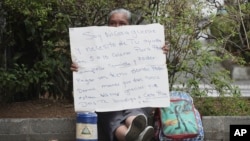 FILE - A Nicaraguan exile, who wishes to only be identified by her nickname "La Profe," Spanish for "the teacher," holds a sign asking for spare change in Alajuela, Costa Rica, March 29, 2019. 