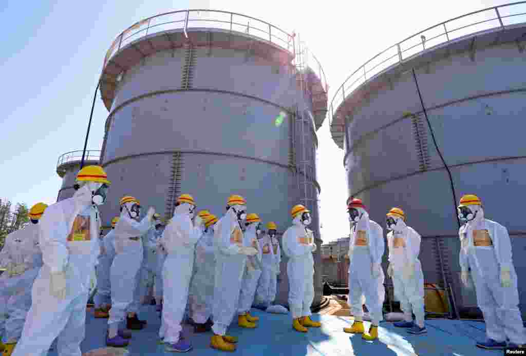 Japan's Prime Minister Shinzo Abe (in red helmet), wearing a protective suit and mask, is briefed about tanks containing radioactive water by Fukushima Daiichi nuclear power plant chief Akira Ono in Okuma, Sept. 19, 2013. 