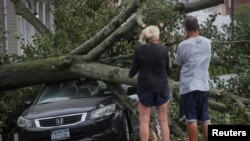 People look at a fallen tree on a car in the aftermath of Tropical Storm Isaias in the Rockaway area of Queens in New York City, Aug. 4, 2020. 