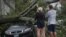 People look at a fallen tree on a car in the aftermath of Tropical Storm Isaias in the Rockaway area of Queens in New York City, Aug. 4, 2020. 