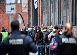 Police stand by as people wearing face masks queue to get access to the vaccination center at the "Arena" in Berlin's Treptow district, Jan 6, 2021.