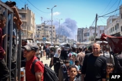 Warga Palestina memadati sebuah jalan sedangkan di belakang tampak asap membubung di Rafah di selatan Jalur Gaza di tengah konflik antara Israel dan kelompok militan Hamas, Selasa, 7 Mei 2024. (Foto: AFP)