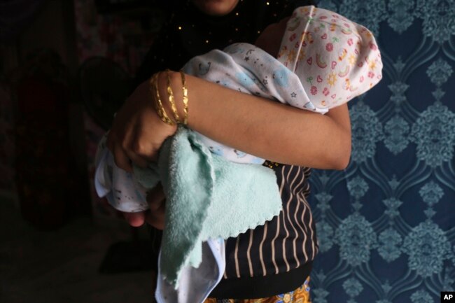 Rohingya child bride, R, age 16, holds her newborn baby while standing in an apartment in Kuala Lumpur, Malaysia, on Oct. 4, 2023. R left Bangladesh's refugee camps for Malaysia in 2022. (AP Photo/Victoria Milko)