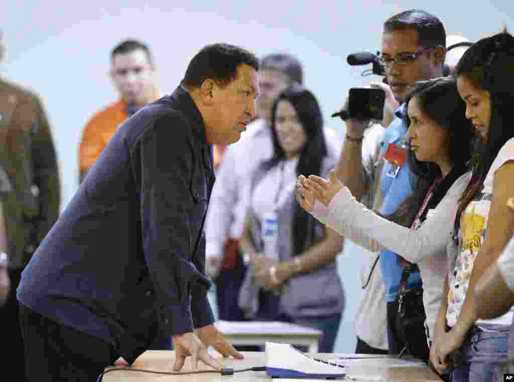 Venezuela's President Hugo Chavez, left, speaks with an electoral worker at a polling station before casting his ballot for the presidential election in Caracas, Venezuela, October 7, 2012. 