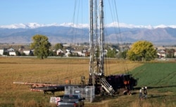 FILE - Workers drill an oil well within sight of houses against a Rocky Mountain backdrop near Longmont, Colorado, October 14, 2014.