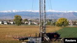 FILE - Workers drill an oil well within sight of houses against a Rocky Mountain backdrop near Longmont, Colorado, Oct. 14, 2014. 