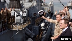 資料照片：時任德國海軍上校的捨恩巴赫（揮帽者）與德國國防部長在吉布提港口為德國海軍護衛艦離港送行（2008年12月23日）
