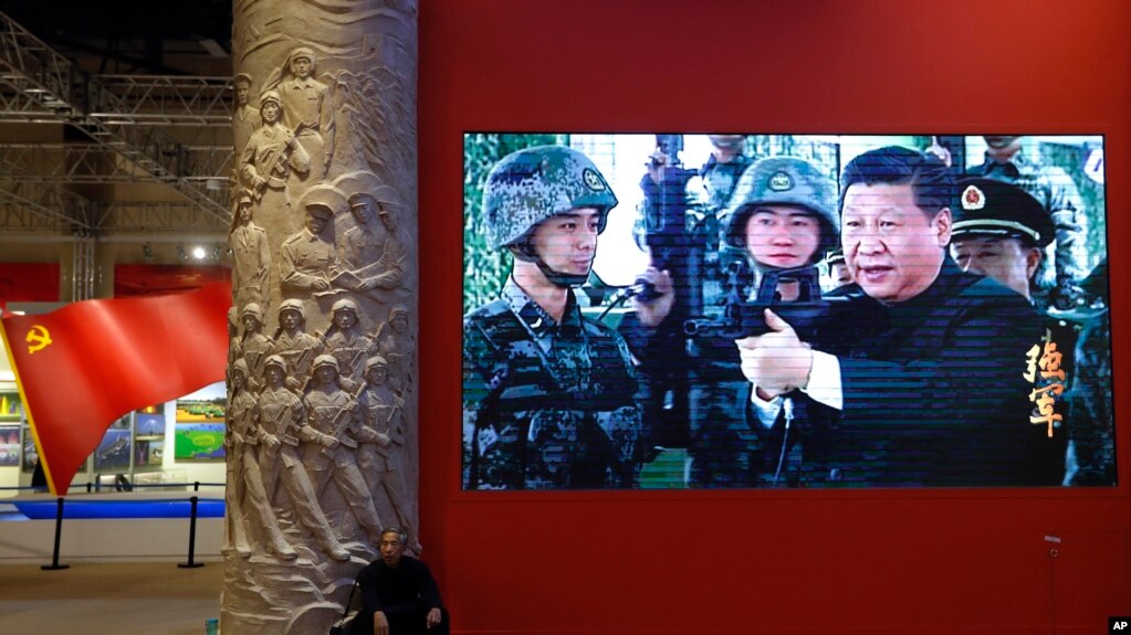 资料照片：2017年10月23日，一名男子在北京的一个视频屏幕旁边休息。视频显示，中国国家主席习近平在北京展览馆举行的一场展览上拿着一支步枪。（美联社照片）(photo:VOA)