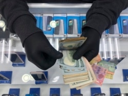 In this Tuesday, April 28, 2020, a cellphone owner shop wears gloves as he counts money on his shop, in Beirut, Lebanon. Public officials and health experts have said that the risk of transferring the virus from person to person through the use of money is minimal. That hasn't stopped businesses from refusing to accept currency, and some countries from urging citizens to stop using banknotes altogether. (AP Photo/Hussein Malla)
