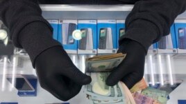 In this Tuesday, April 28, 2020, a cellphone owner shop wears gloves as he counts money on his shop, in Beirut, Lebanon. Public officials and health experts have said that the risk of transferring the virus from person to person through the use of money is minimal. That hasn't stopped businesses from refusing to accept currency, and some countries from urging citizens to stop using banknotes altogether. (AP Photo/Hussein Malla)