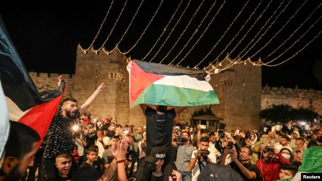 Warga Palestina mengibarkan bendera di luar Gerbang Damaskus, Yerusalem Minggu malam (25/4) setelah penghalang yang dipasang polisi Israel, dilepas.