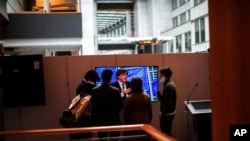 People gather around a television set showing an interview with Member of European Parliament Carles Puigdemont at the European Parliament in Brussels, March 9, 2021. 