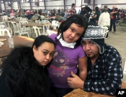 FILE - Wildfire survivors Marolyn Romero-Sim, left, with Hugo Romero-Rodriguez, center, and their 9-year-old daughter, Milagros, sit inside the evacuation center at the Ventura County Fairgrounds in Ventura, Calif., Dec. 6, 2017.