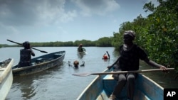 FILE: Fatou Jatta, right, holds her paddle as she works with her colleagues to catch fish and crabs from the mangrove in the estuary waters of the Gambia river in Serrekunda, Gambia. 9.25.2021