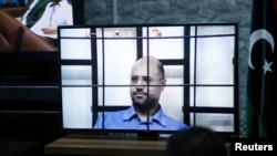 Saif al-Islam Gadhafi, son of deposed leader Muammar Gadhafi, is seen on a screen via video-link in a courtroom in Tripoli, Libya, as he attends a hearing behind bars in a courtroom in Zintan, April 27, 2014. 