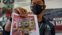 A officer shows a wanted poster displaying two militants Ali Kalora, top left, and Jaka Ramadan, bottom left, in Indonesia, Sept. 19, 2021. 