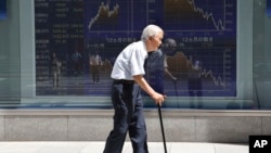 FILE - An elderly man walks by an electronic stock board of a securities firm in Tokyo, Aug. 19, 2016.