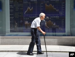 FILE - An elderly man walks by an electronic stock board of a securities firm in Tokyo, Aug. 19, 2016.