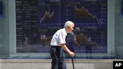 An elderly man walks by an electronic stock board of a securities firm in Tokyo, Aug. 19, 2016.