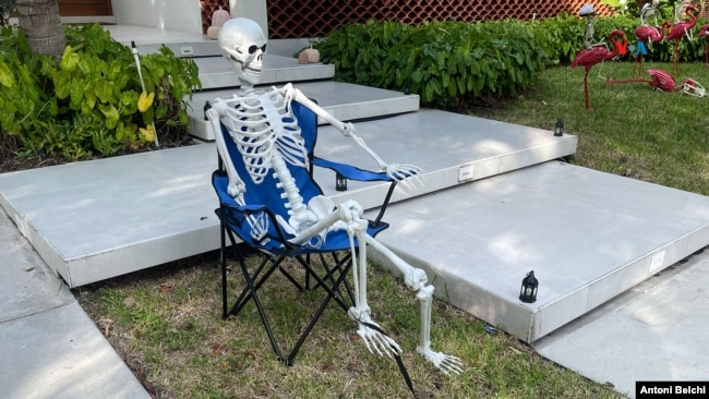 Una figura de un esqueleto sentado en una silla frente a una casa como parte de la decoración de Halloween en un barrio de Miami, Florida. (Foto: Antoni Belchi / VOA)