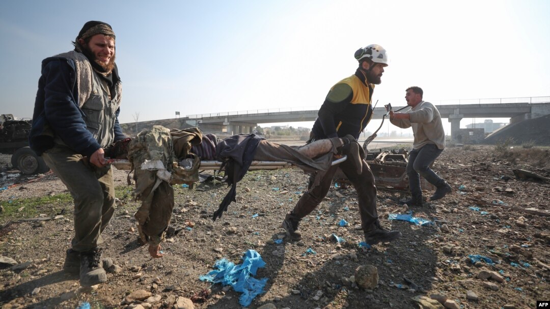 Un rescatista de los Cascos Blancos de Siria y un civil transportan el cuerpo de una víctima tras un ataque aéreo ruso en la autopista Damasco-Alepo cerca de Maaret añ-Numan en Idlib, en el sur del país, el 22 de diciembre de 2019. AFP/Haj Kadour.