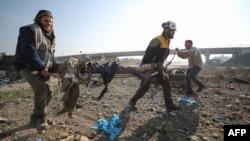 Un rescatista de los Cascos Blancos de Siria y un civil transportan el cuerpo de una víctima tras un ataque aéreo ruso en la autopista Damasco-Alepo cerca de Maaret añ-Numan en Idlib, en el sur del país, el 22 de diciembre de 2019. AFP/Haj Kadour.