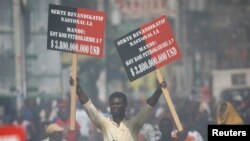 A protester holds placards during a march to demand an investigation into what they say is the alleged misuse of Venezuela-sponsored PetroCaribe funds, in Port-au-Prince, Haiti, Oct. 17, 2018.