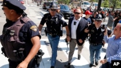 FILE - In this Tuesday, July 19, 2016 file photo, Alex Jones, center right, is escorted by police out of a crowd of protesters outside the Republican convention in Cleveland. Facebook says it has taken down four pages belonging to conspiracy theorist Alex Jones for violating its hate speech and bullying policies. The social media giant said in a statement Monday, Aug. 6, 2018 that it also blocked Jones' account for 30 days because he repeatedly posted content that broke its rules. (AP Photo/John Minchillo, File)