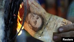 Un hombre quema un billete de 100 bolívares durante una protesta en El Pinal, Venezuela.