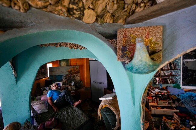 Nissim Kahlon gets up from his bed in his home chiseled out of the sandstone cliffs overlooking the Mediterranean sea in Herzliya, Israel, Wednesday, June 28, 2023. (AP Photo/Ariel Schalit)