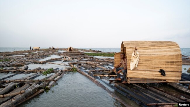 Egontoluwa Marigi, 61, sits in his shelter on his grouping of logs, while transporting the logs from Ondo State to Lagos State on the Lagos Lagoon, Nigeria on December 1, 2021. (REUTERS/Nyancho NwaNri)