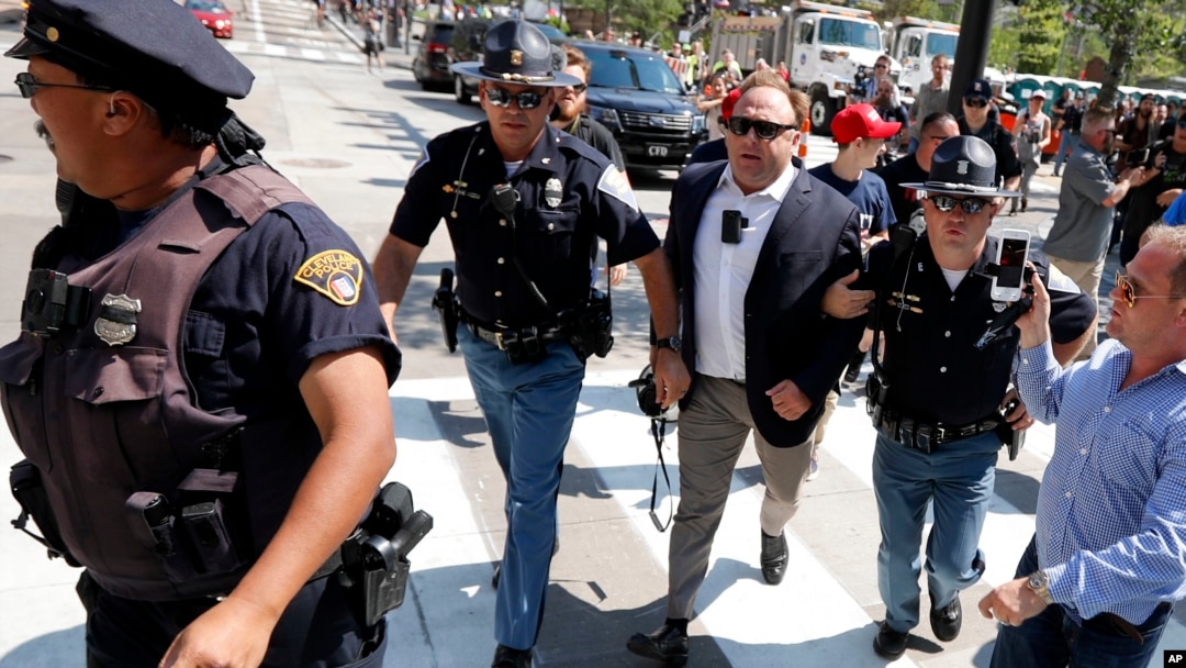 El teorista de conspiraciones Alex Jones (centro) es escoltado por la policía de entre una multitud que protestaba afuera de la convención republicana en Cleveland, el 169de julio de 2016. Facebook anunció que ha cerrado cuatro páginas de Jones por violar sus normas sobre discursos de odio y acoso.