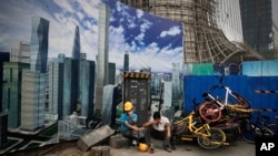 ILE- In this June 26, 2018, file photo Chinese workers take a break outside a construction site wall depicting the skyscrapers in the Chinese capital at the Central Business District in Beijing.