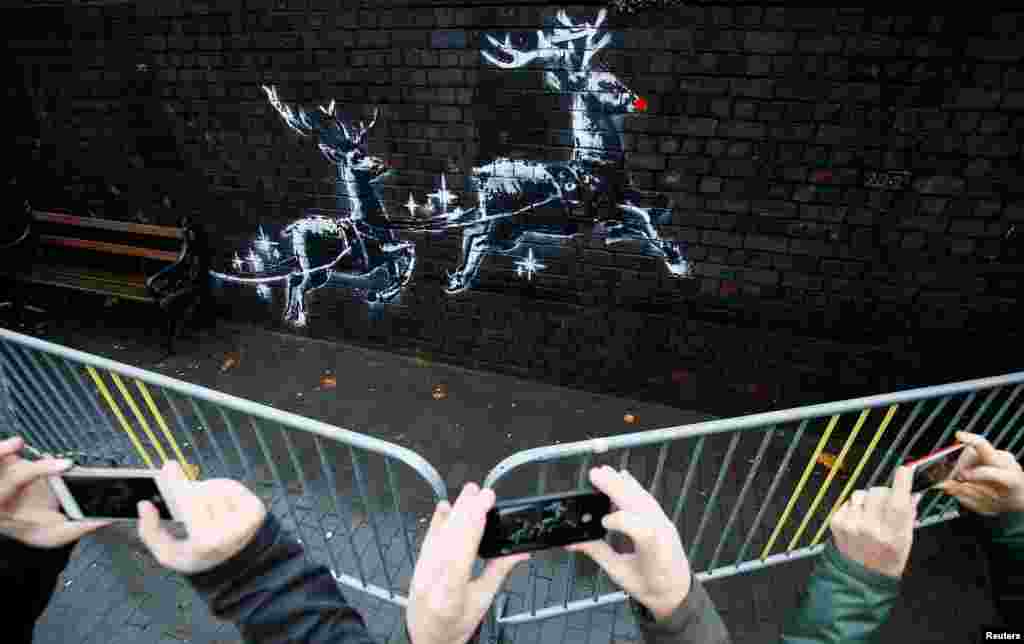 People gather round a new mural by the street artist Banksy in Birmingham, Britain.