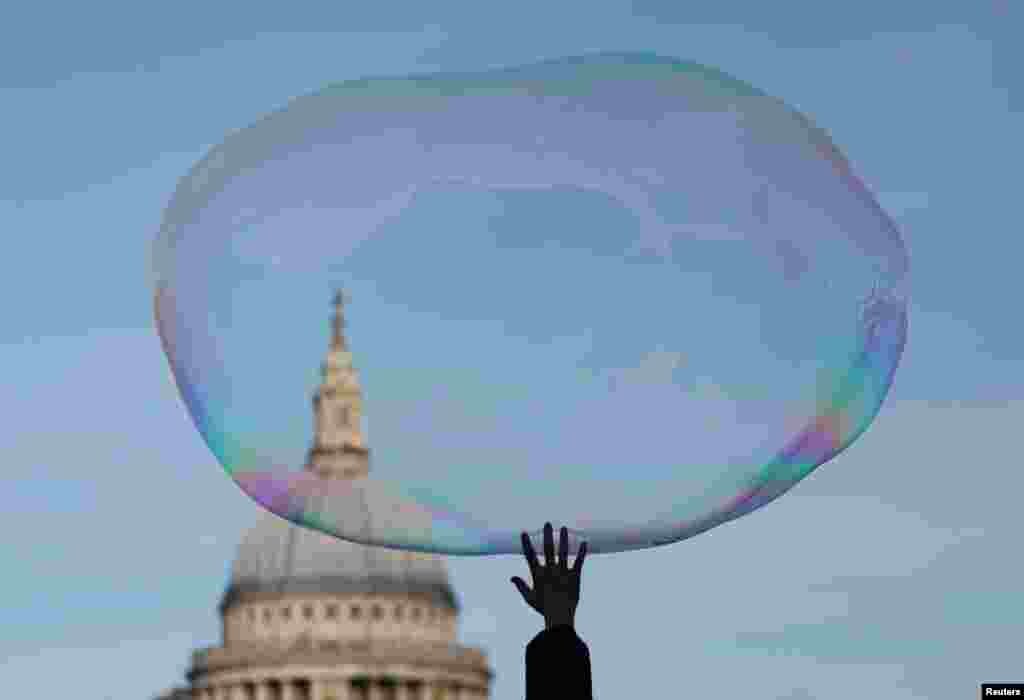 A child bursts a soap bubble as it floats past St Paul&#39;s Cathedral in London, Britain.