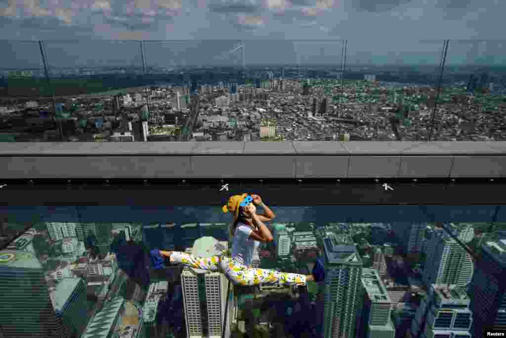 A woman wearing a face mask observes a partial solar eclipse on the Mahanakhon Skywalk Glass Tray at the King Power Mahanakhon building in Bangkok, Thailand.