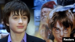 Aktor Daniel Radcliffe berpose untuk fotografer di samping foto dirinya di pemutaran perdana film "Harry Potter and the Philosopher's Stone" di New York pada 11 November 2001. (Foto: Reuters)