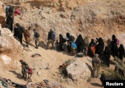 FILE - Islamic state fighters and their families walk as they surrender in the village of Baghouz, Deir el Zour province, Syria, March 12, 2019.