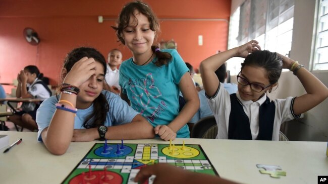 In this Friday, Oct. 13, 2017 photo, girls play a board game at the Ramon Marin Sola Elementary School, which opened its doors as a daytime community center after the passing of Hurricane Maria in Guaynabo, Puerto Rico. (AP Photo/Carlos Giusti)