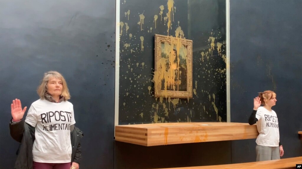 En esta imagen tomada de un video, dos activistas climáticas permanecen de pie y con una mano en alto luego de arrojar sopa al vidrio que protege la Mona Lisa, el domingo 28 de enero de 2024, en el Museo del Louvre, en París.