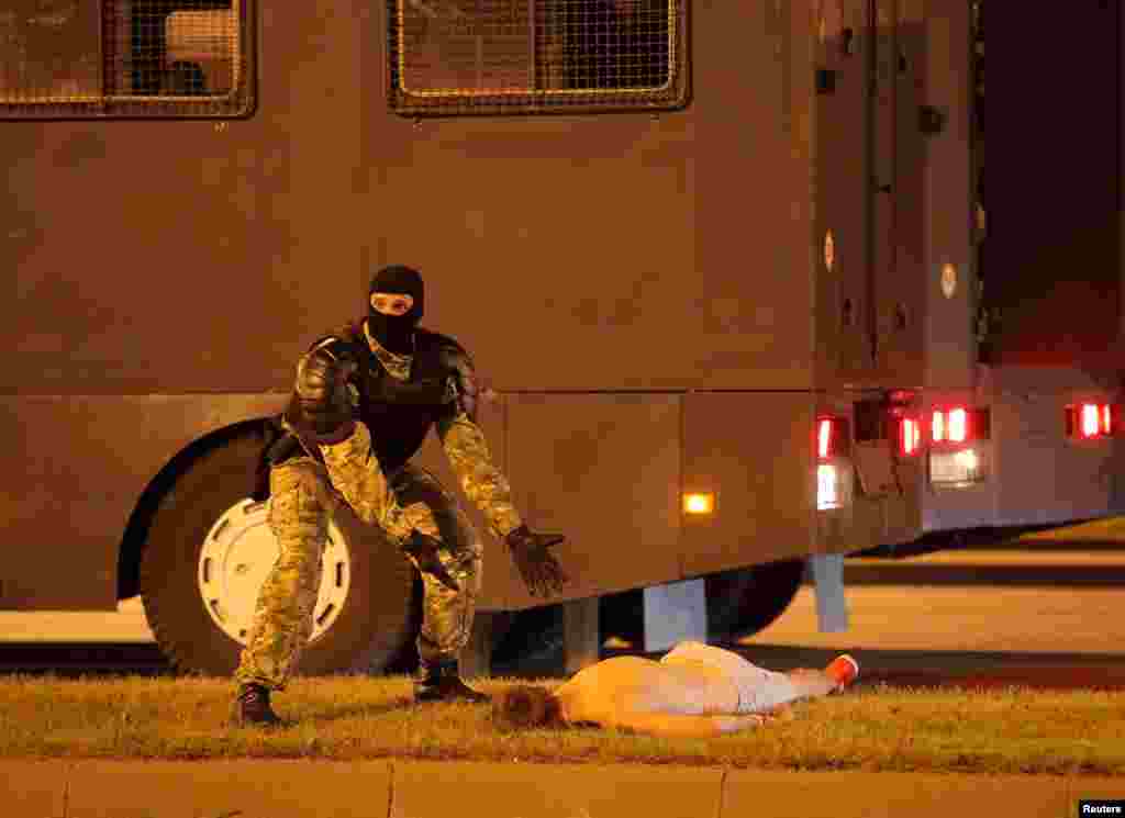 A Belarusian law enforcement officer gestures next to an injured protester Yevgeny Zaichkin during clashes after presidential election polls closed in Minsk, Belarus, Aug. 9, 2020.