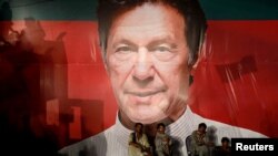 Des ouvriers s'assoient sous un mur avec un panneau d'affichage d'Imran Khan, président du parti politique pakistanais Tehreek-e-Insaf (PTI), Karachi.