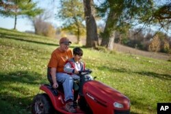 Caroline Clarin rides with Ali Patan, 7, as he drives her riding mower at her home in Dalton, Minn., Oct. 30, 2021.